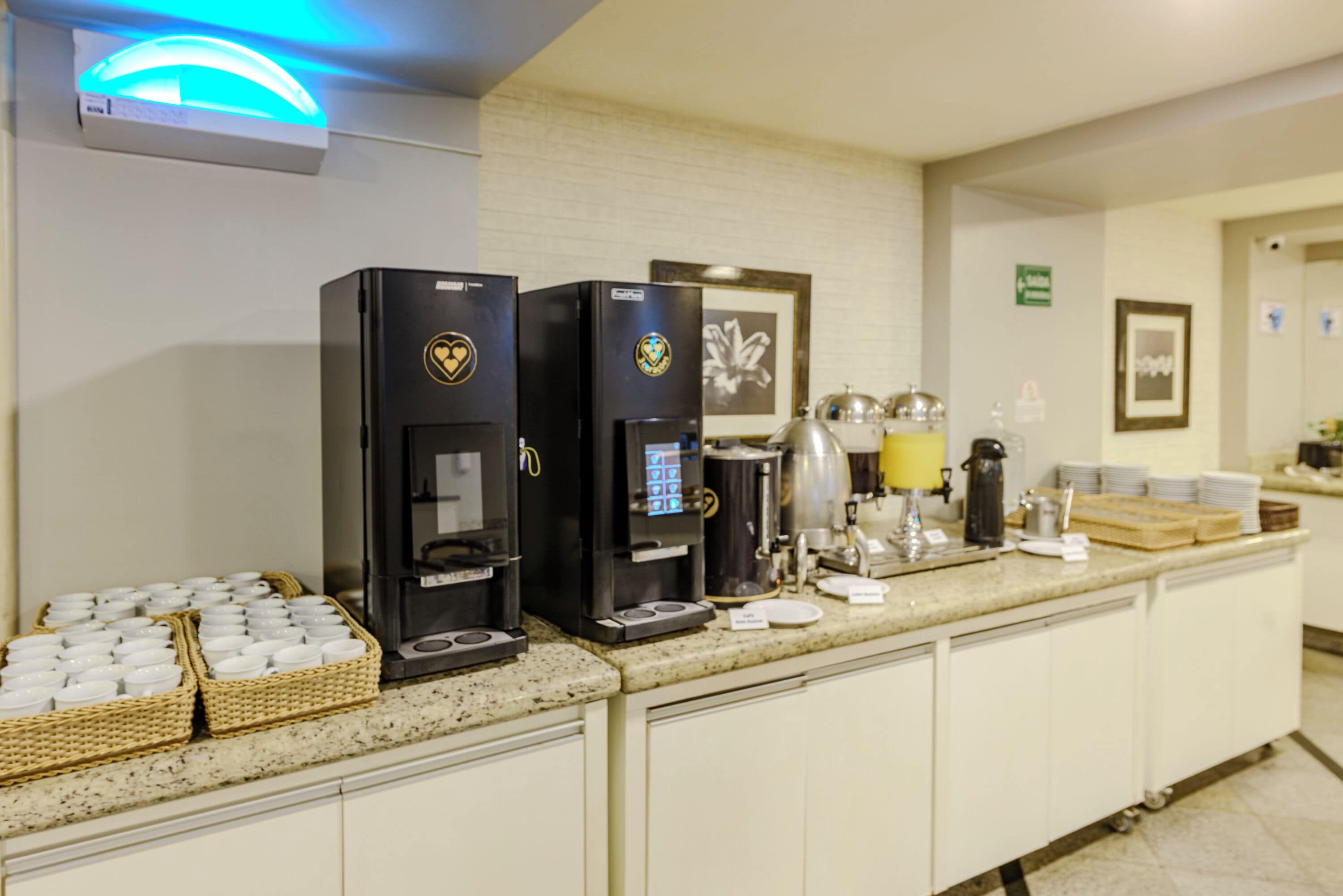 Una postazione self-service con caffè, dotata di due macchine da caffè, cestini con bicchieri usa e getta e diversi accessori per la preparazione.
