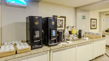 Una postazione self-service con caffè, dotata di due macchine da caffè, cestini con bicchieri usa e getta e diversi accessori per la preparazione.