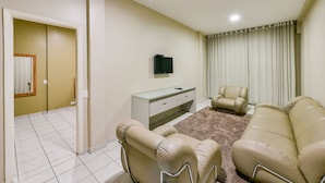 A living room with a sofa, a chair, a TV, and a desk. - Plaza Inn Augustus - Downtown (Goiania)