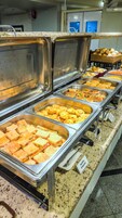 Buffet com diversas opções de comida, incluindo pães, muffins e doces.