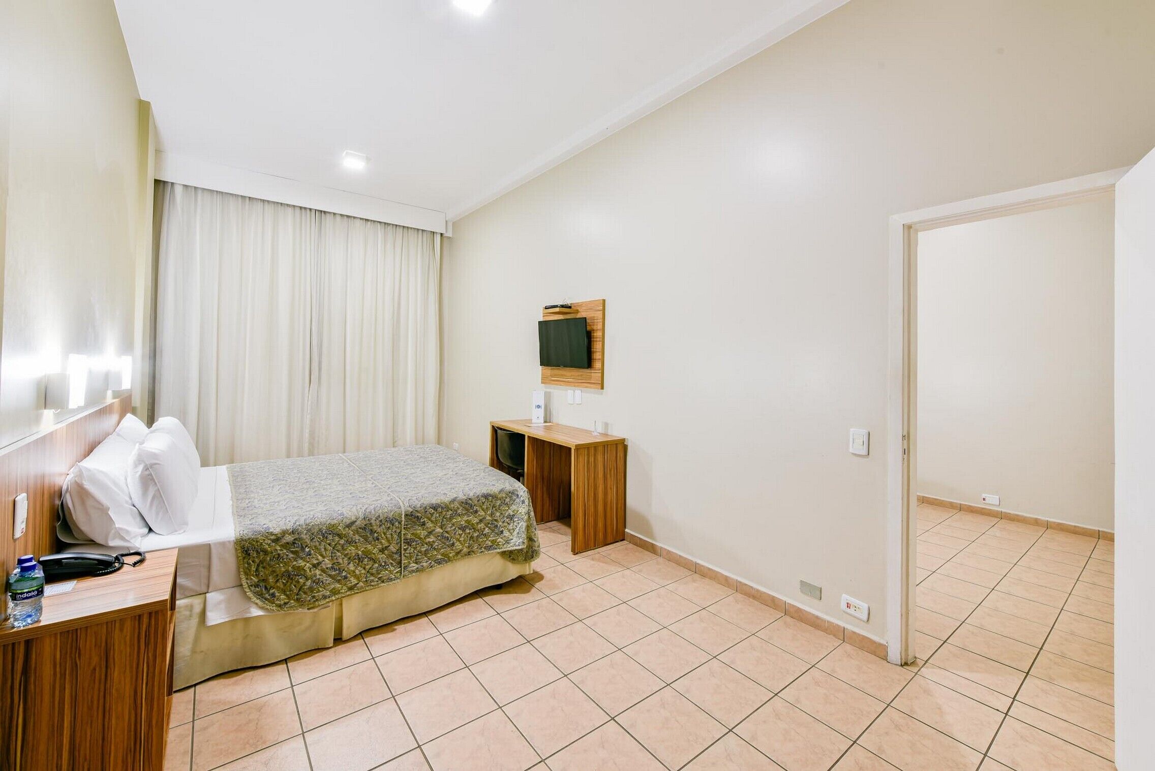 Una habitación de hotel con cama, mesita de noche, televisor y puerta.