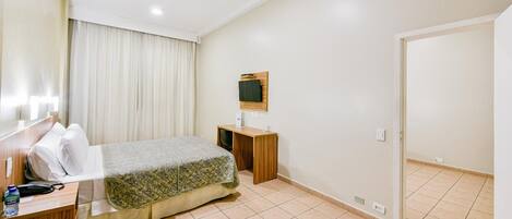 Una habitación de hotel con cama, mesita de noche, televisor y puerta.