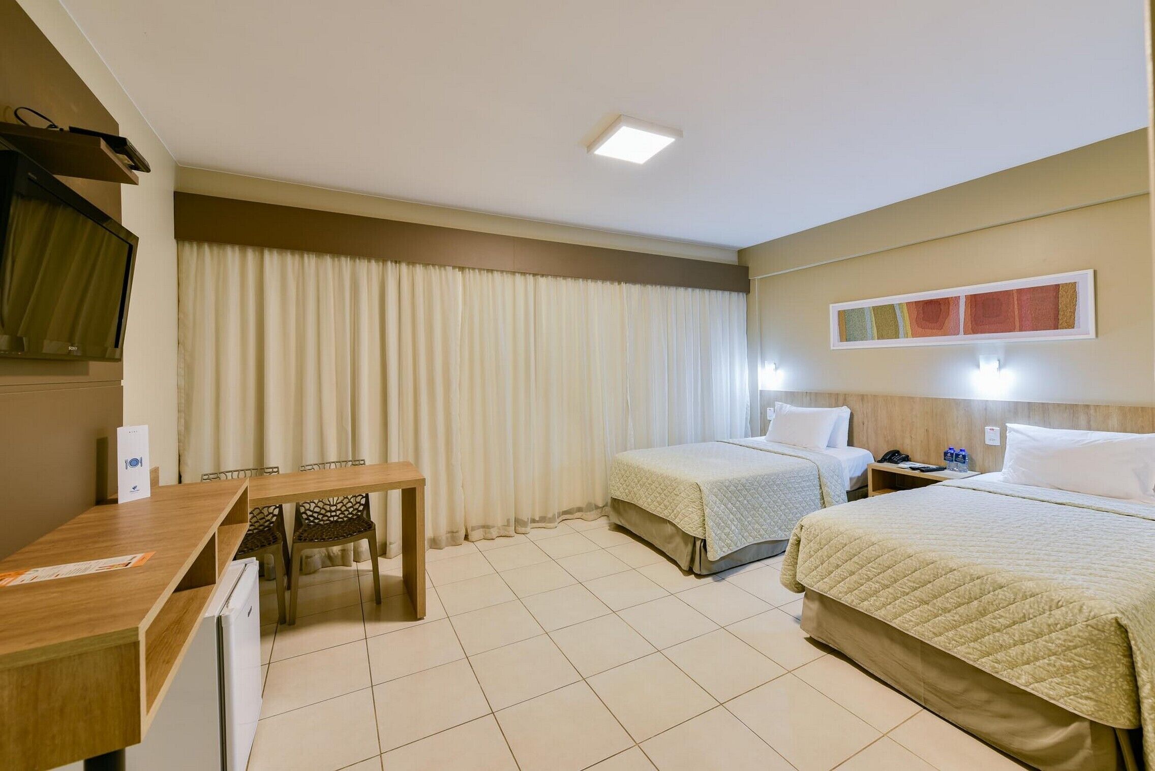 Habitación de hotel con dos camas, un escritorio, una silla, un televisor y una ventana con cortinas.
