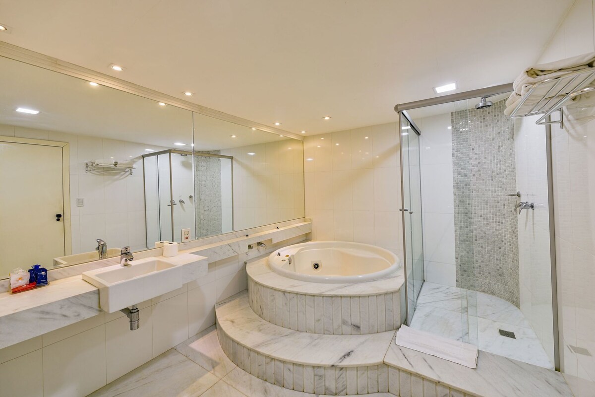 A modern bathroom with a large mirror, two sinks, a freestanding bathtub, and a glass-enclosed shower area.