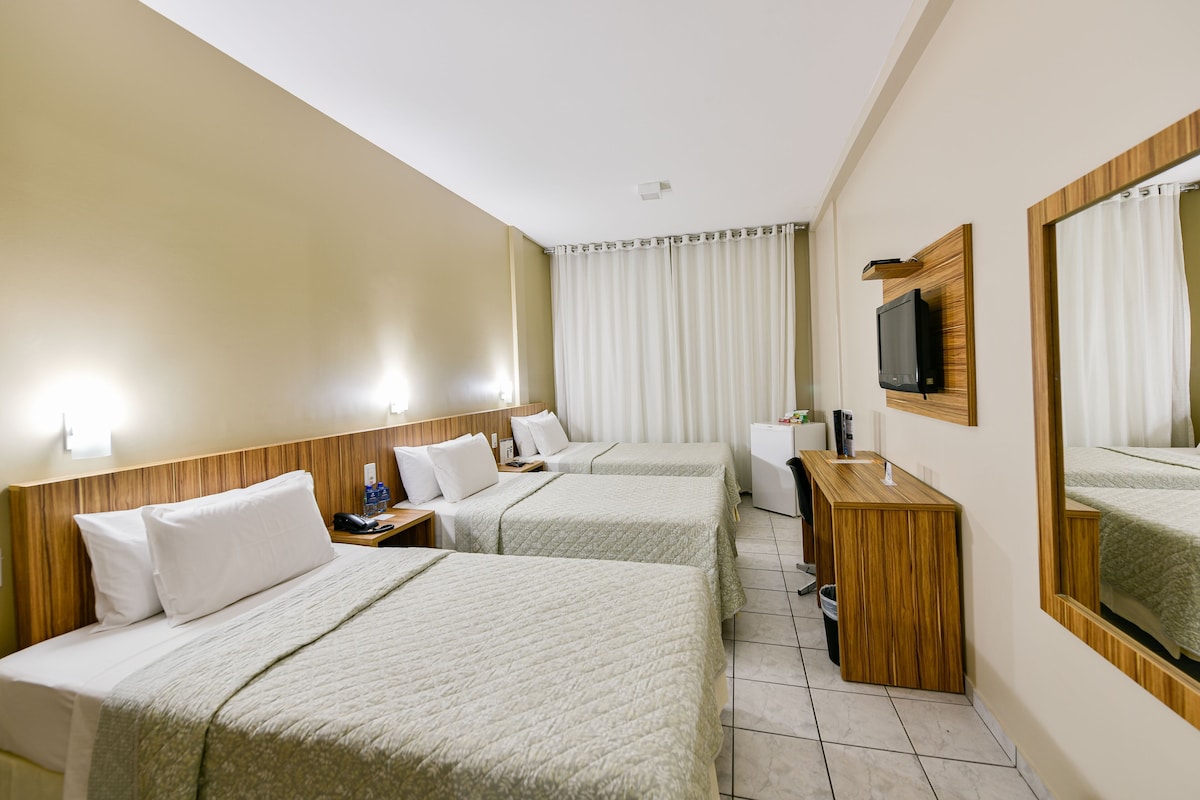 A hotel room with two beds, a desk, a television, and a window with curtains.