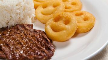 A plate with white rice, fried dough rings, a grilled steak, and a glass of orange juice.