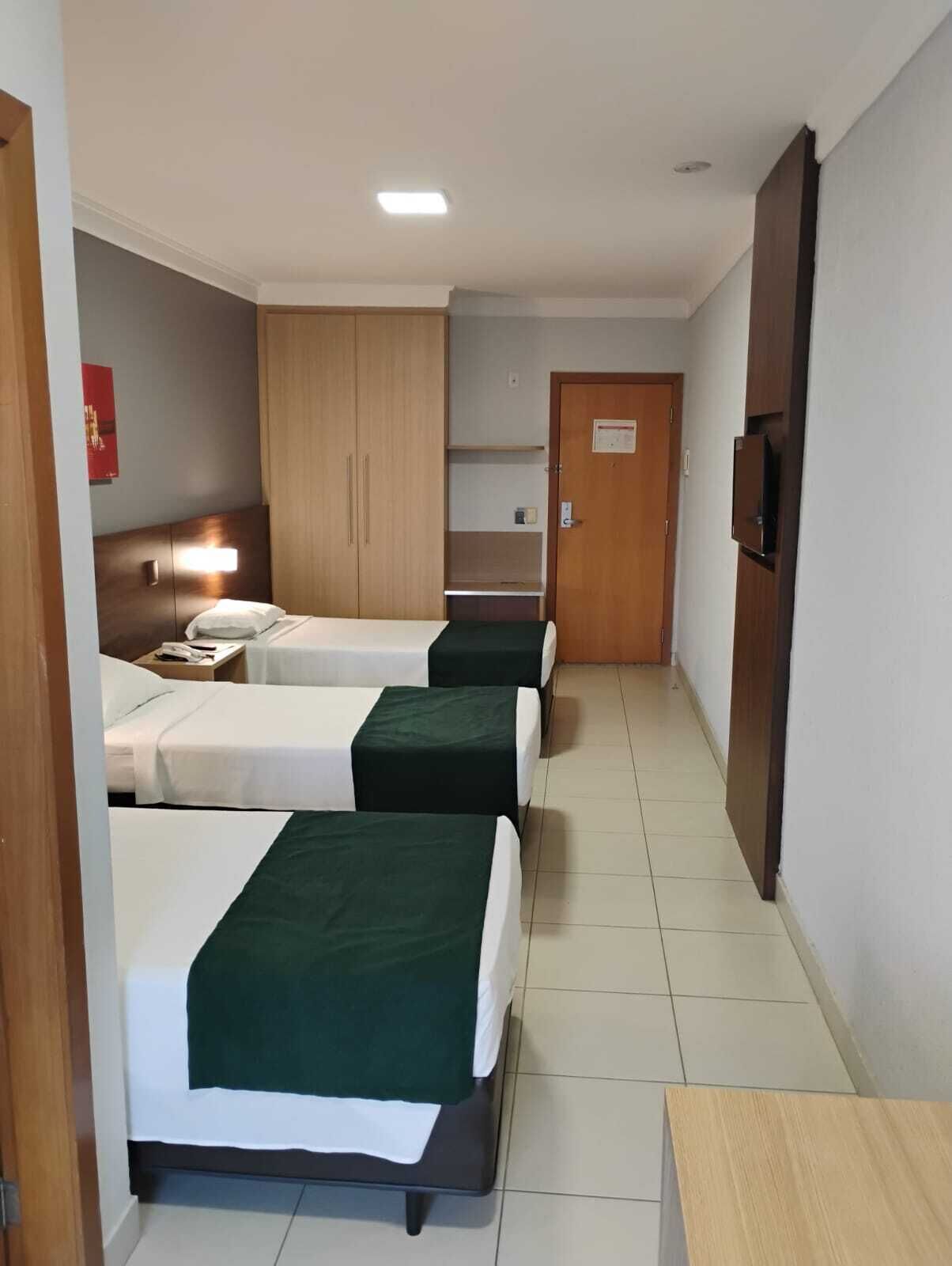 A hotel room with three beds, a wooden wardrobe, a television, and a small table.