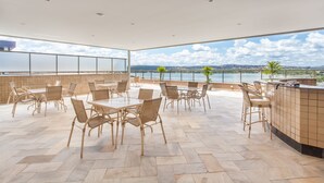 A spacious outdoor dining area with wicker chairs and a tiled floor, overlooking a body of water and distant landscape. - Transamerica Lagoa Santa (Lagoa Santa)