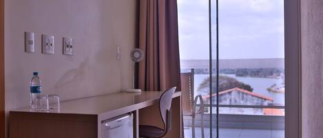 Habitación de hotel con escritorio, silla y vistas a una masa de agua a través de amplias ventanas.