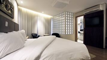A hotel room with a large bed, a desk, a chair, a TV, and a bathroom visible through an open door.
