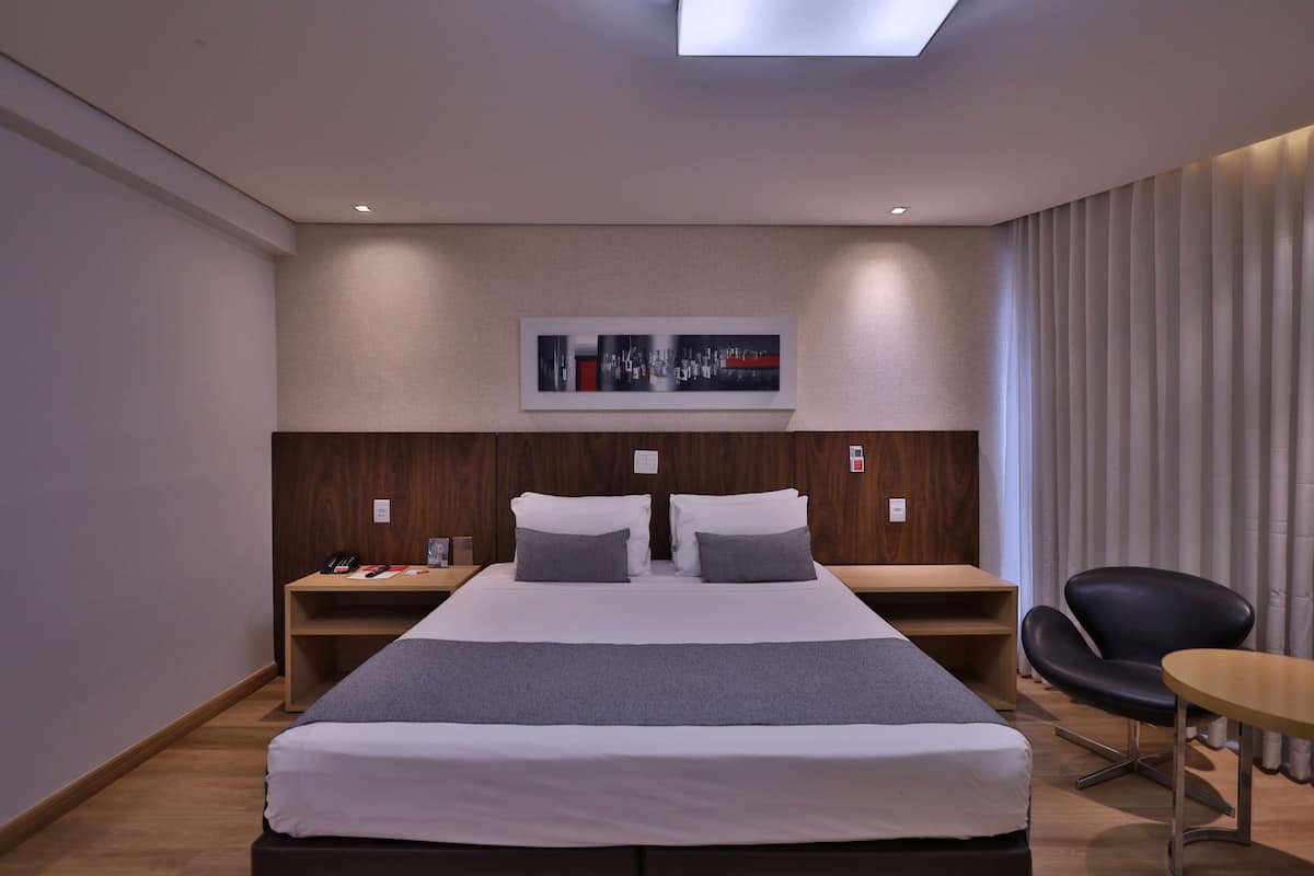A modern hotel room with a large bed, two bedside tables, a desk, a chair, and a ceiling light.
