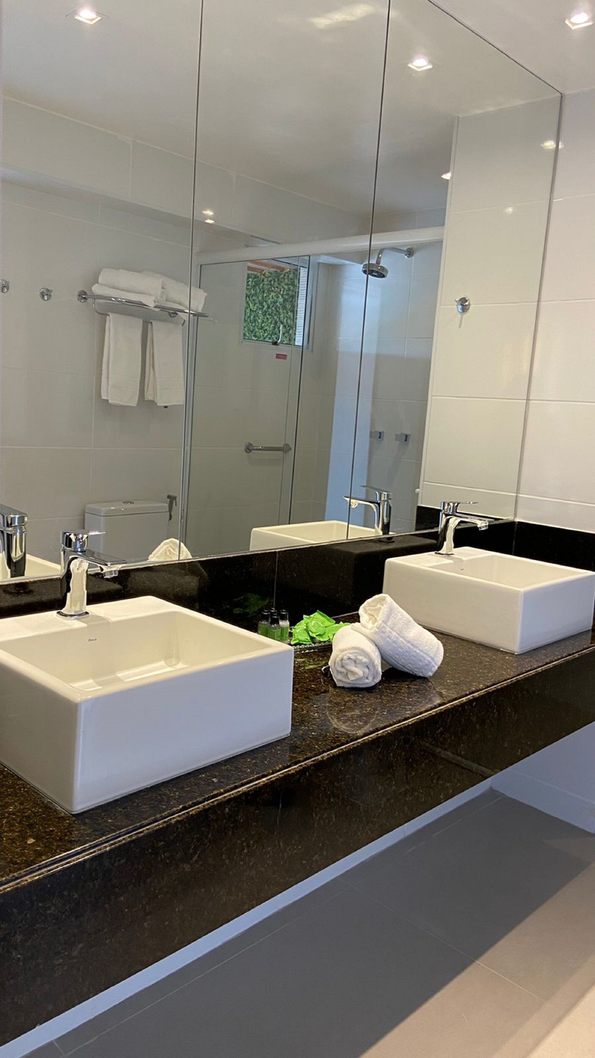 Un baño moderno con dos lavamanos blancos, un espejo grande y una cabina de ducha de vidrio.