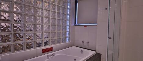 Ein modernes Badezimmer mit Duschkabine aus Glas, einer großzügigen Badewanne und einer gefliesten Wand mit Glasbauelementen.