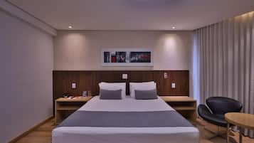 Habitació d'hotel moderna amb un llit gran, capçalera de fusta, taules de nit, un escriptori, una cadira i una làmpada al sostre.
