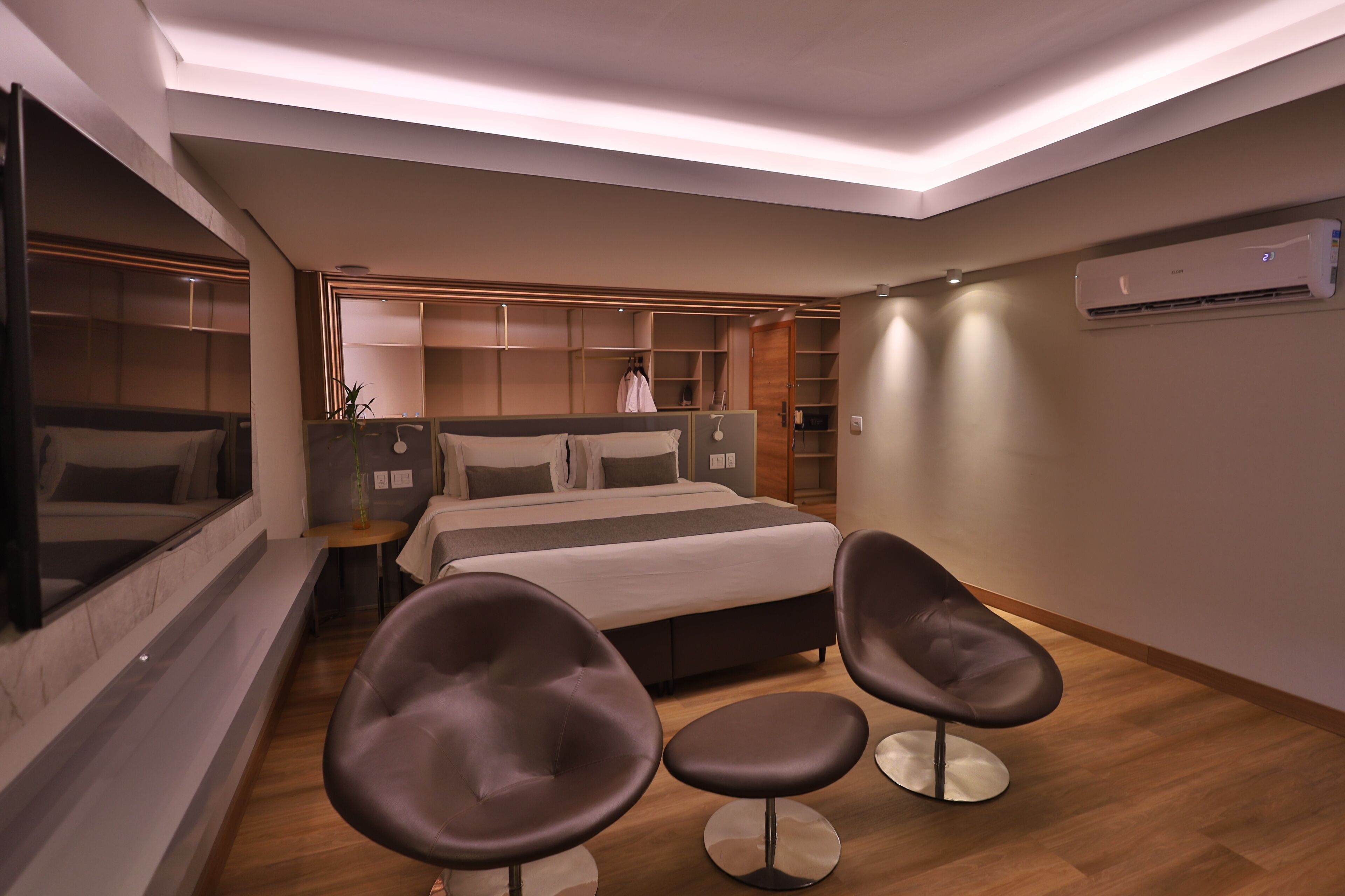 Ett modernt hotellrum med en stor säng, två fåtöljer, ett sängbord, en spegel och inbyggd förvaring.