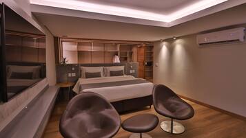 Ein modernes Hotelzimmer mit einem großen Bett, zwei Sesseln, einem Nachttisch, einem Spiegel und integrierten Stauraum.