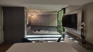 A modern hotel room with a large bed, a TV mounted on the wall, a small seating area with a table and chairs, and a view of the cityscape through the window. - Transamerica Lagoa Santa (Lagoa Santa)