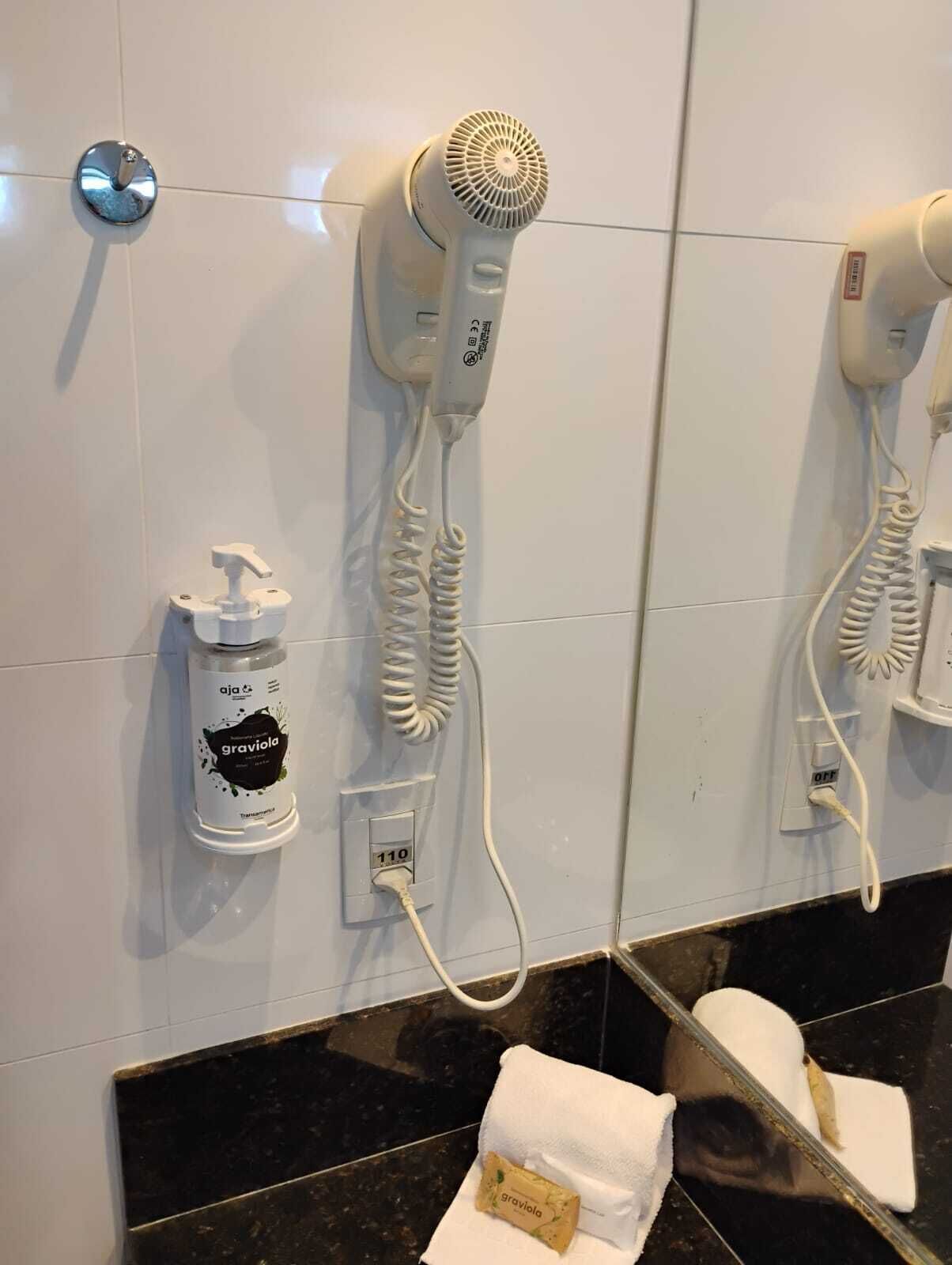 A bathroom with two hair dryers mounted on the wall, a bottle of shampoo, and towels on the floor.
