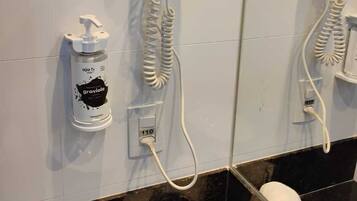 A bathroom with two hair dryers mounted on the wall, a bottle of shampoo, and towels on the floor.