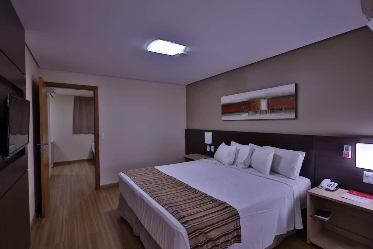 A hotel room with a bed, bedside table, and a flat-screen TV.