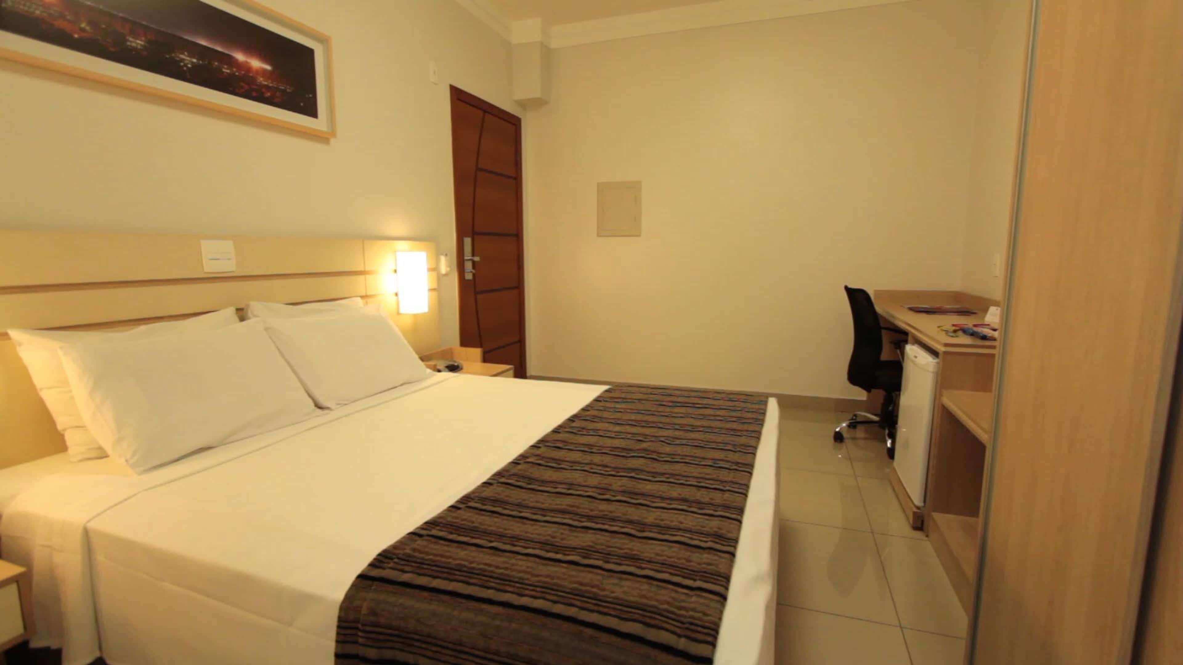 A hotel room with a bed, a desk, and a chair.