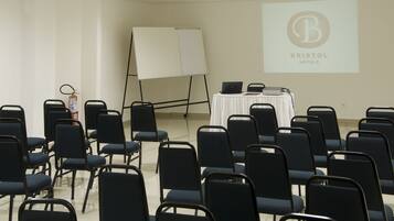 A conference room with rows of chairs, a whiteboard, a laptop on a table, and a projector screen displaying the Bristol Hotels logo.