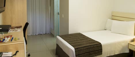 Ein Hotelzimmer mit einem Bett, einem Schreibtisch mit Computer, einem Stuhl und einem fensterbepflegten Fenster.