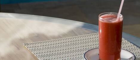 Un verre d’une boisson rouge est posé sur une table recouverte d’un set de table en fibres tressées, près d’une piscine.