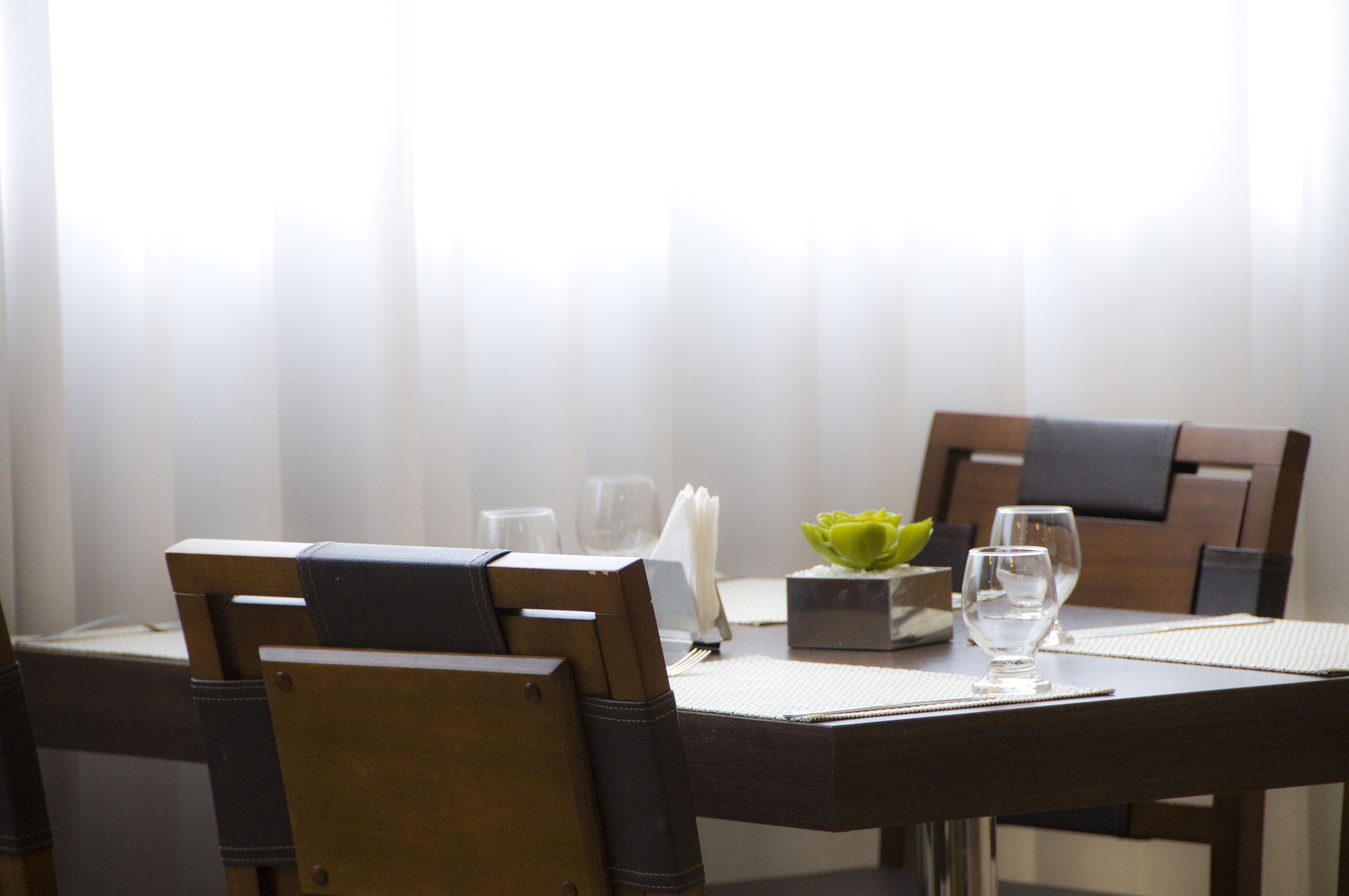 A dining table set with chairs, a vase with a green flower, and a small box.