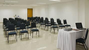 Ein Konferenzraum mit Reihen von Stühlen, einem Tisch mit Laptop und Projektor sowie einer Tür im Hintergrund.