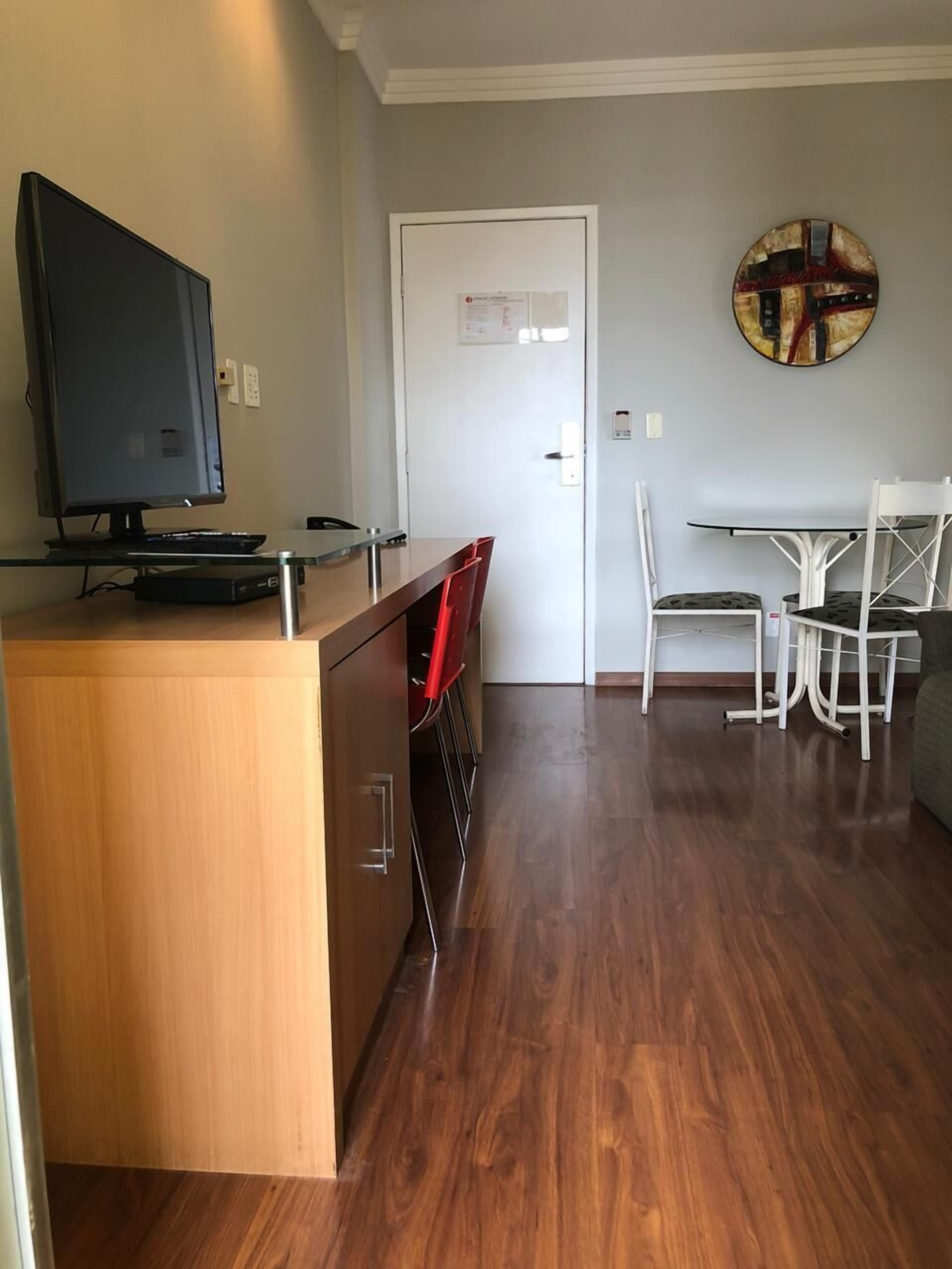 A modern living room with a wooden entertainment unit, a flat-screen TV, and a dining area with white chairs and a table.