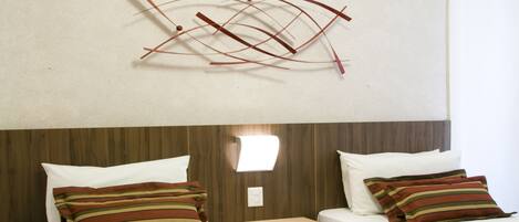Habitación de hotel con dos camas, cada una con ropa de cama y almohadas a rayas, un cabecero de madera, un aire acondicionado de pared y una lámpara sencilla.
