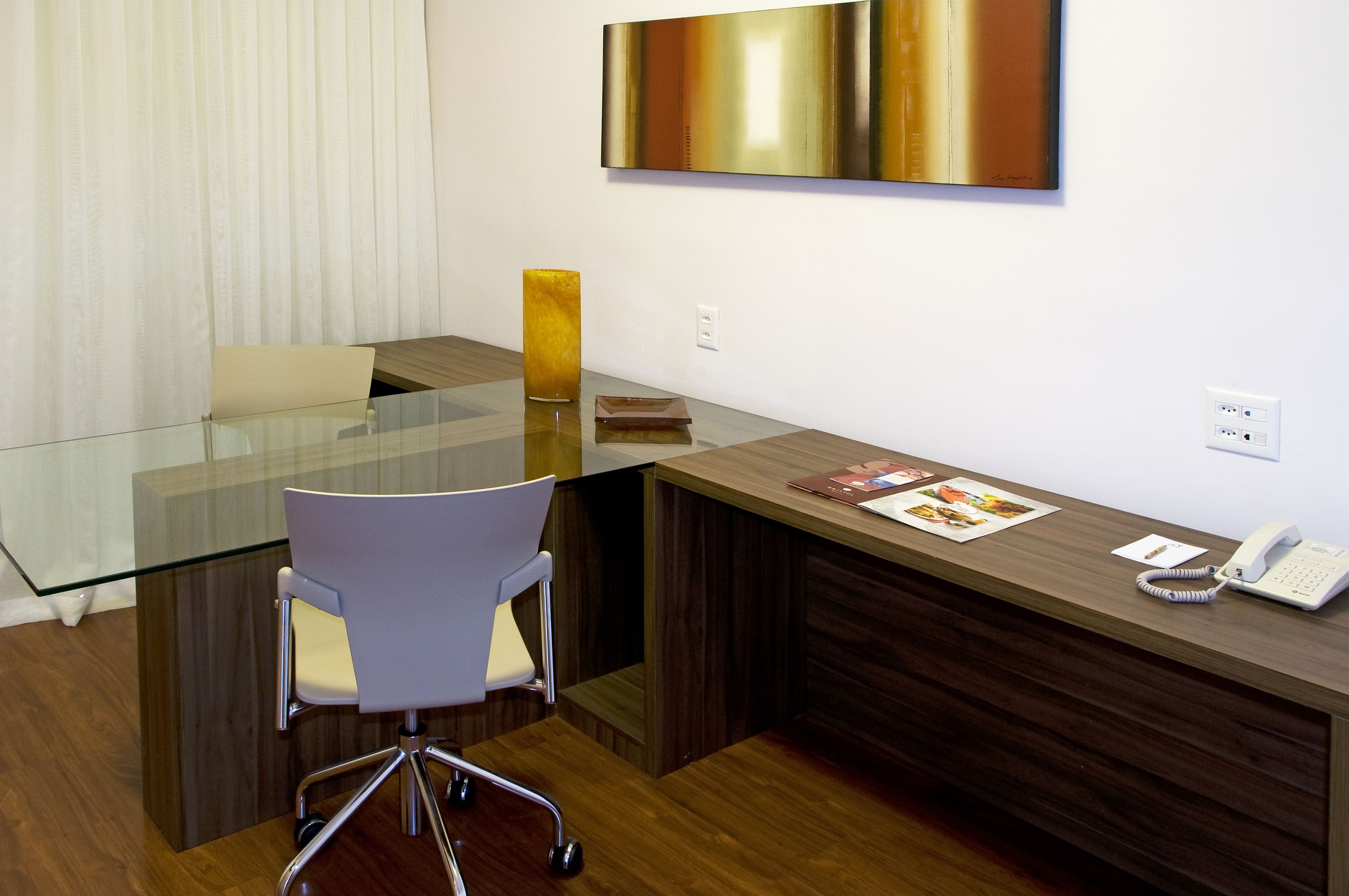 A modern office with a glass table, white chair, wooden reception desk, and a large abstract painting on the wall.