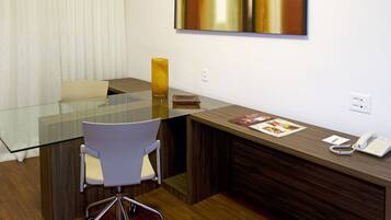 A modern office with a glass table, white chair, wooden reception desk, and a large abstract painting on the wall.