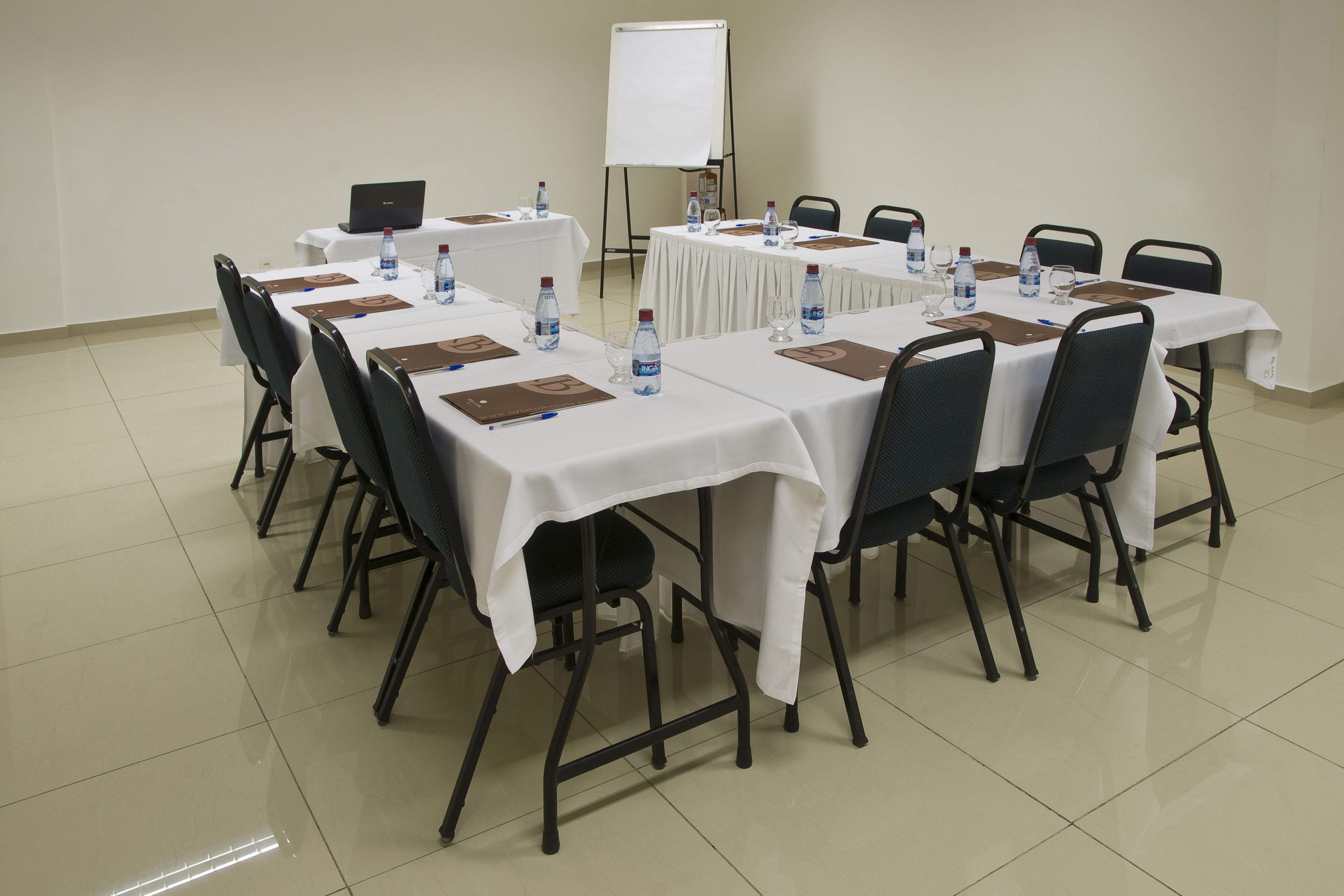 Un salón de conferencias con mesas dispuestas para reuniones, equipado con computadoras portátiles, botellas de agua y tarjetas de identificación.