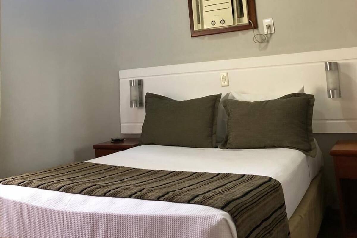 Een hotelkamer met een bed, een nachtkastje, een wandlamp en een plafondlamp.