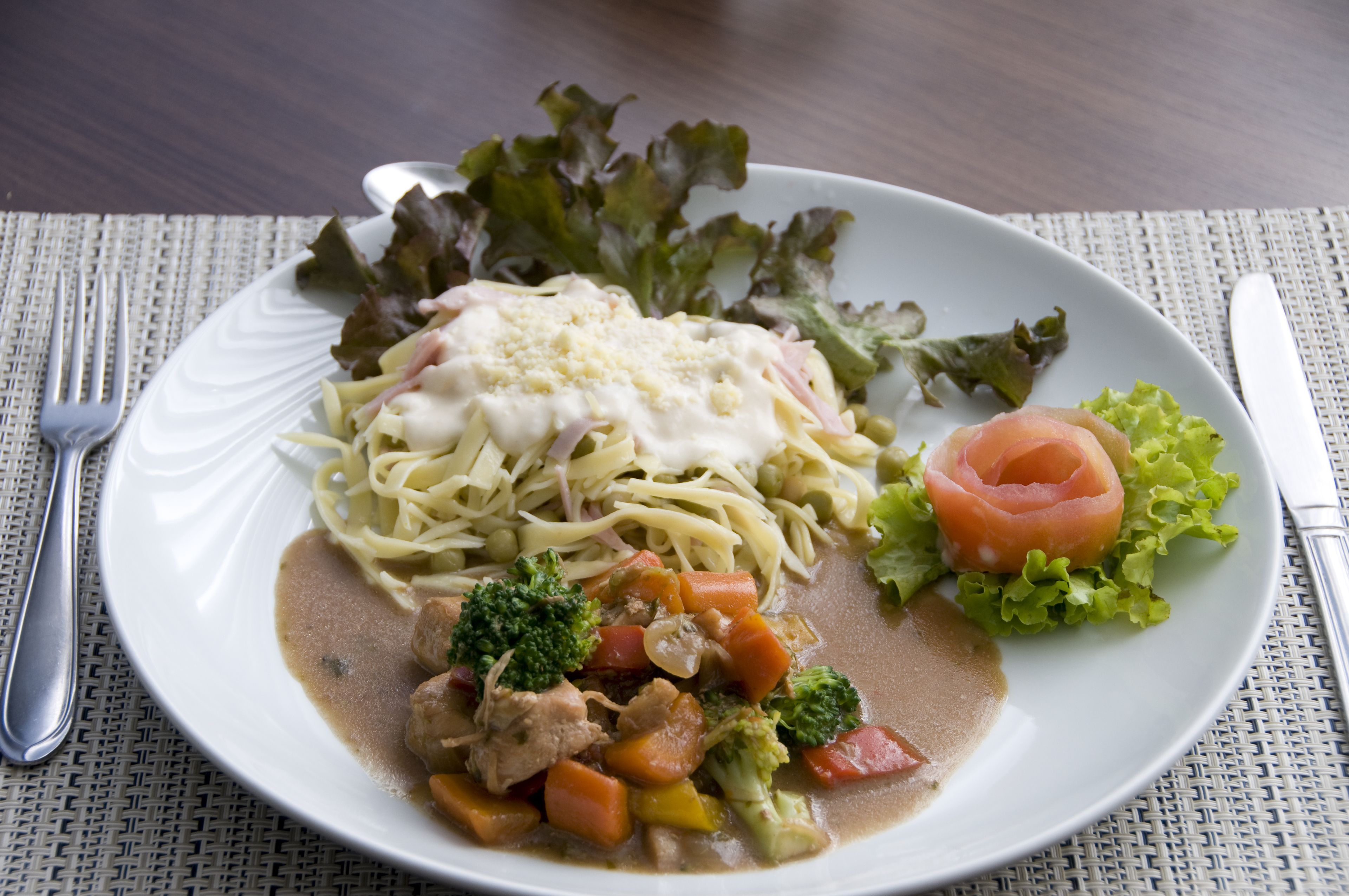 A plate of food with pasta, vegetables, and a slice of salmon on a white plate.