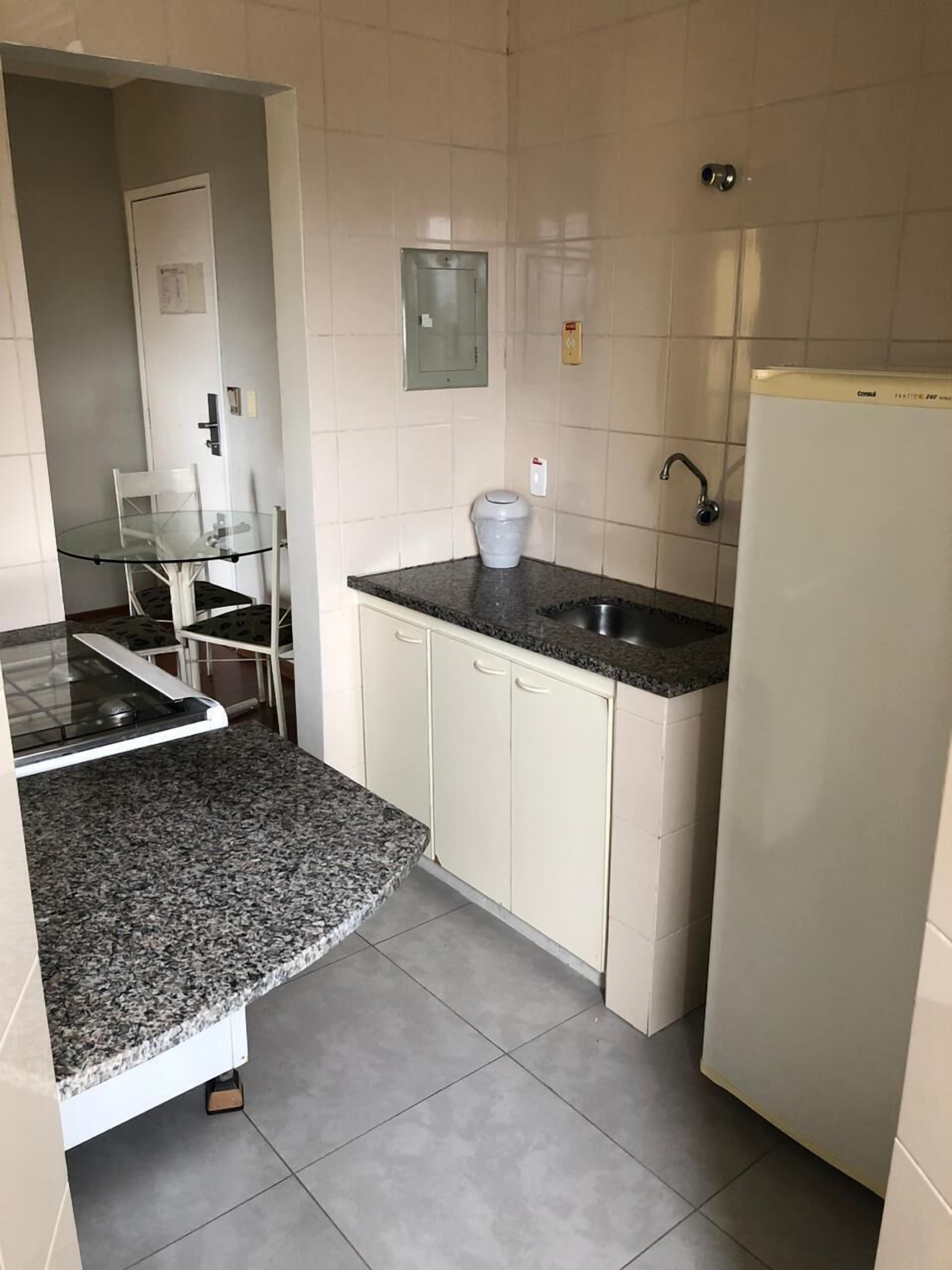 Une cuisine compacte dotée d’un plan de travail en granit, de meubles blancs, d’un four encastré et d’un réfrigérateur.