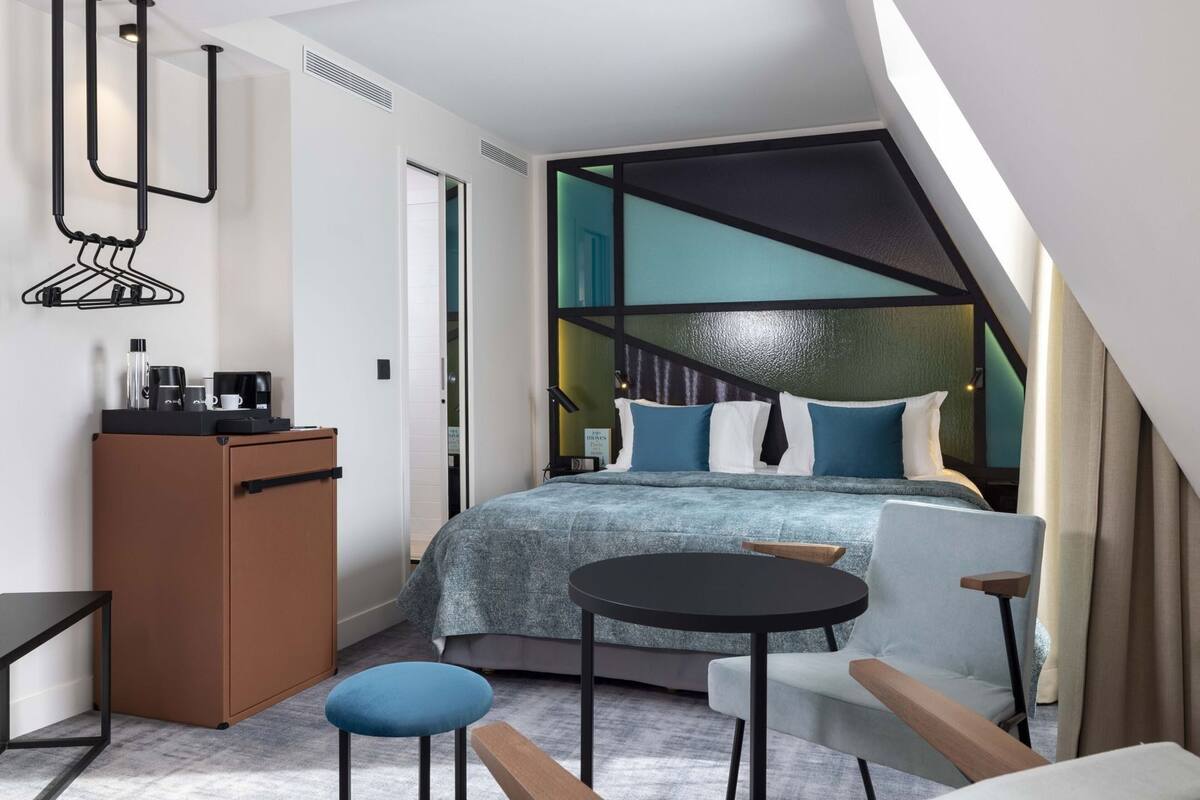 A compact hotel room with a bed, a desk, a chair, and a small table.