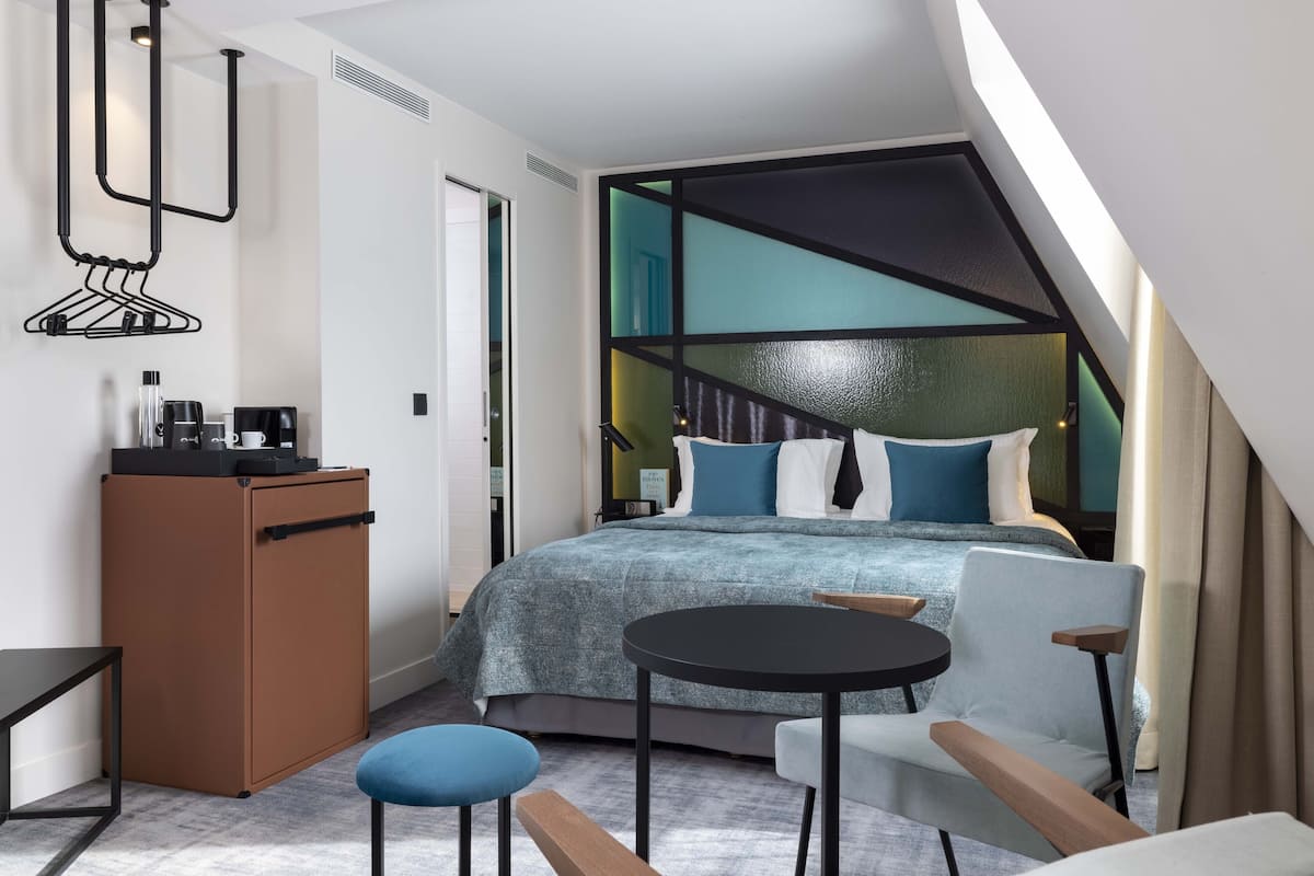 A modern hotel room with a bed, a desk, a chair, and a small table.