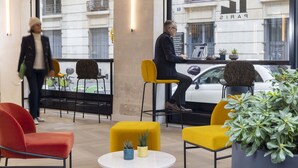 A modern interior with yellow and red chairs, a round table, and a large window with a view of a white car and a building with 'PARIS' signage. - Le 12 Hotel (Paris)