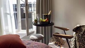 A room with a view of a balcony, a small table with a basket of fruit and a bottle of champagne, a leopard print throw, and a pair of sunglasses on a chair. - Le 12 Hotel (Paris)