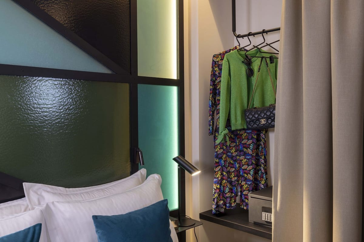 A hotel room with a bed, pillows, a hanging wardrobe, and a microwave on the counter.