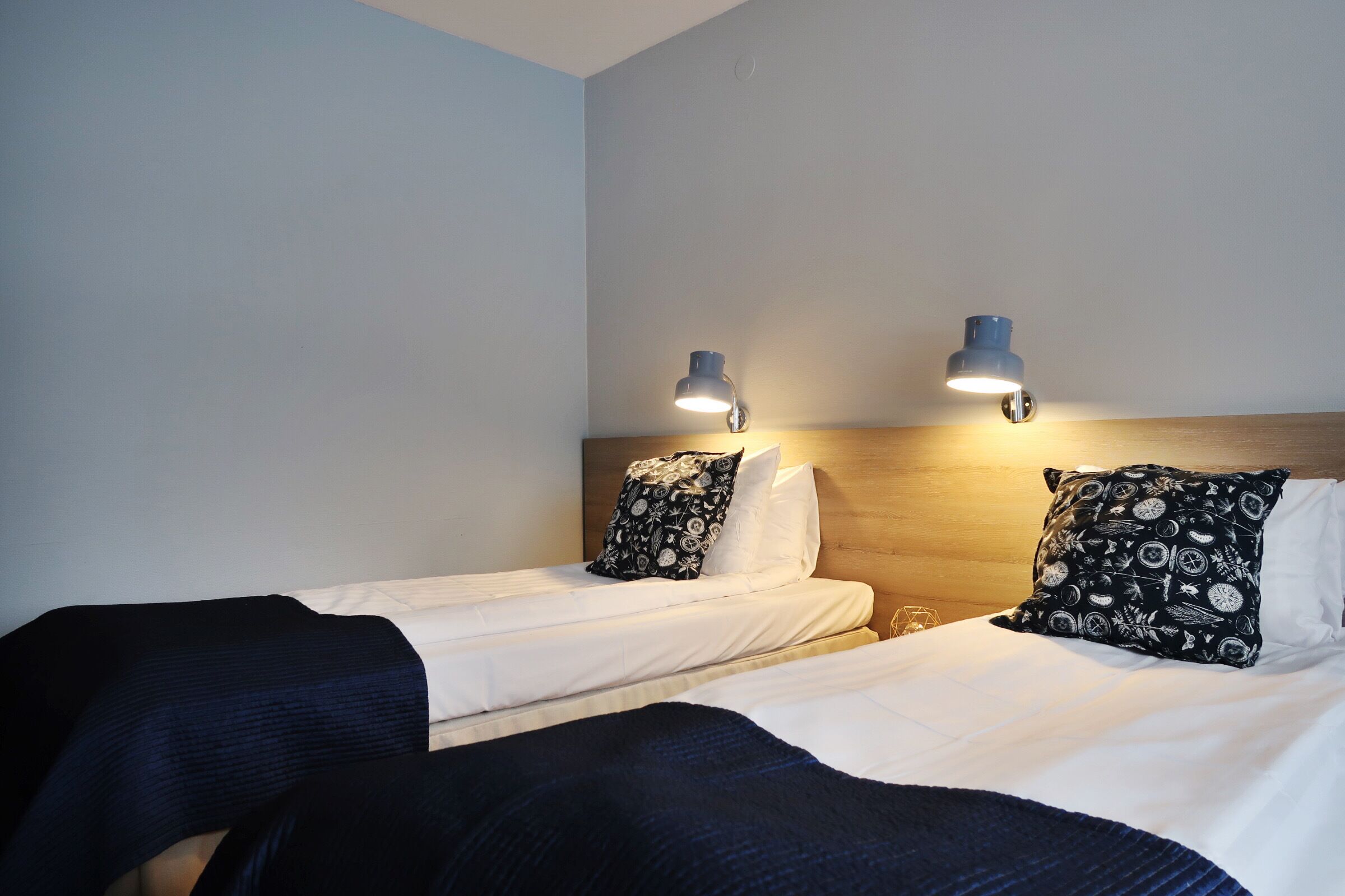 Una camera d'albergo con due letti singoli, ciascuno con un cuscino decorato e una lampada da comodino.