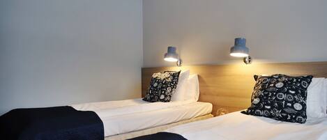 Una camera d'albergo con due letti singoli, ciascuno con un cuscino decorato e una lampada da comodino.