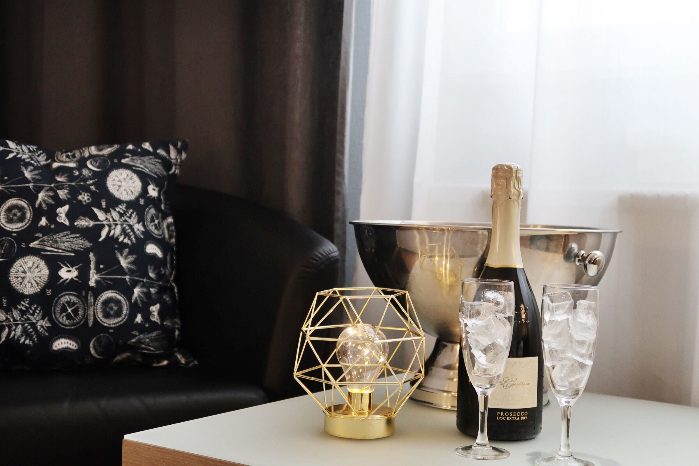 Une table avec une bouteille de Prosecco, deux coupes de champagne et un luminaire décoratif.