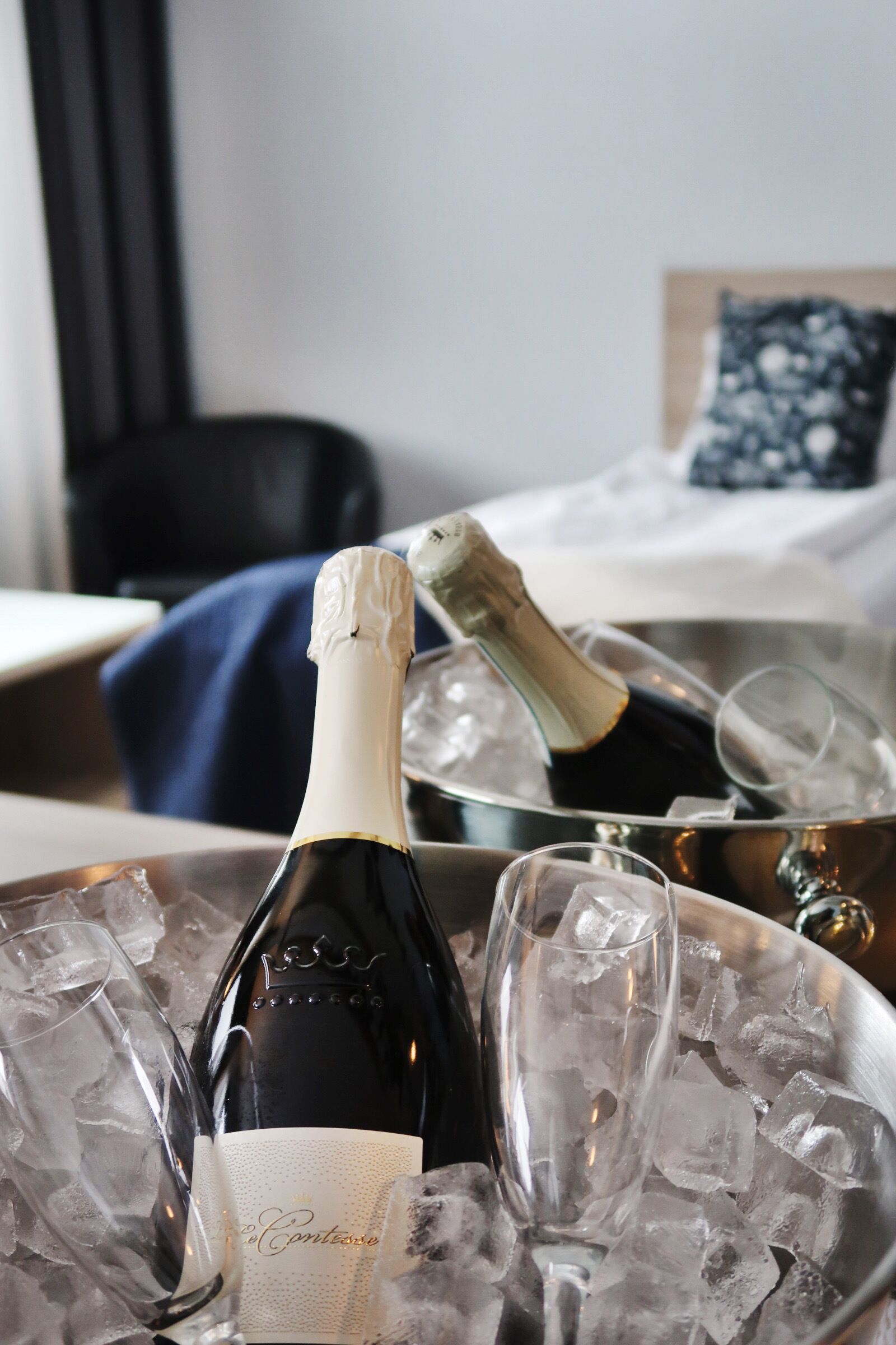 A bottle of champagne and a glass in a metal bucket filled with ice, placed on a table in a hotel room.