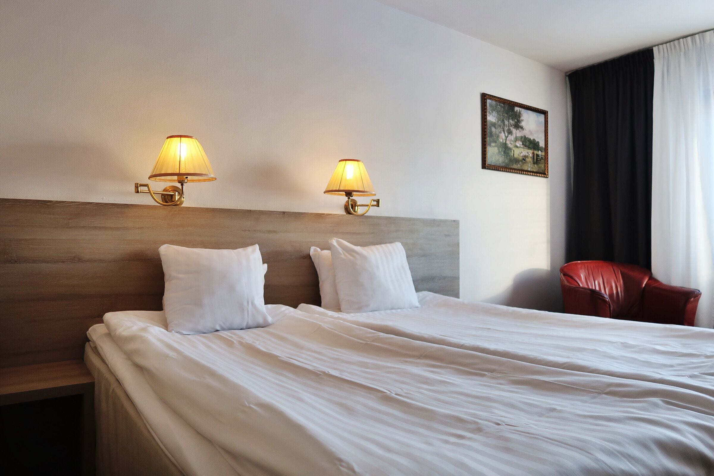 Une chambre d’hôtel avec un grand lit, deux lampes de chevet, un fauteuil rouge et un tableau au mur.