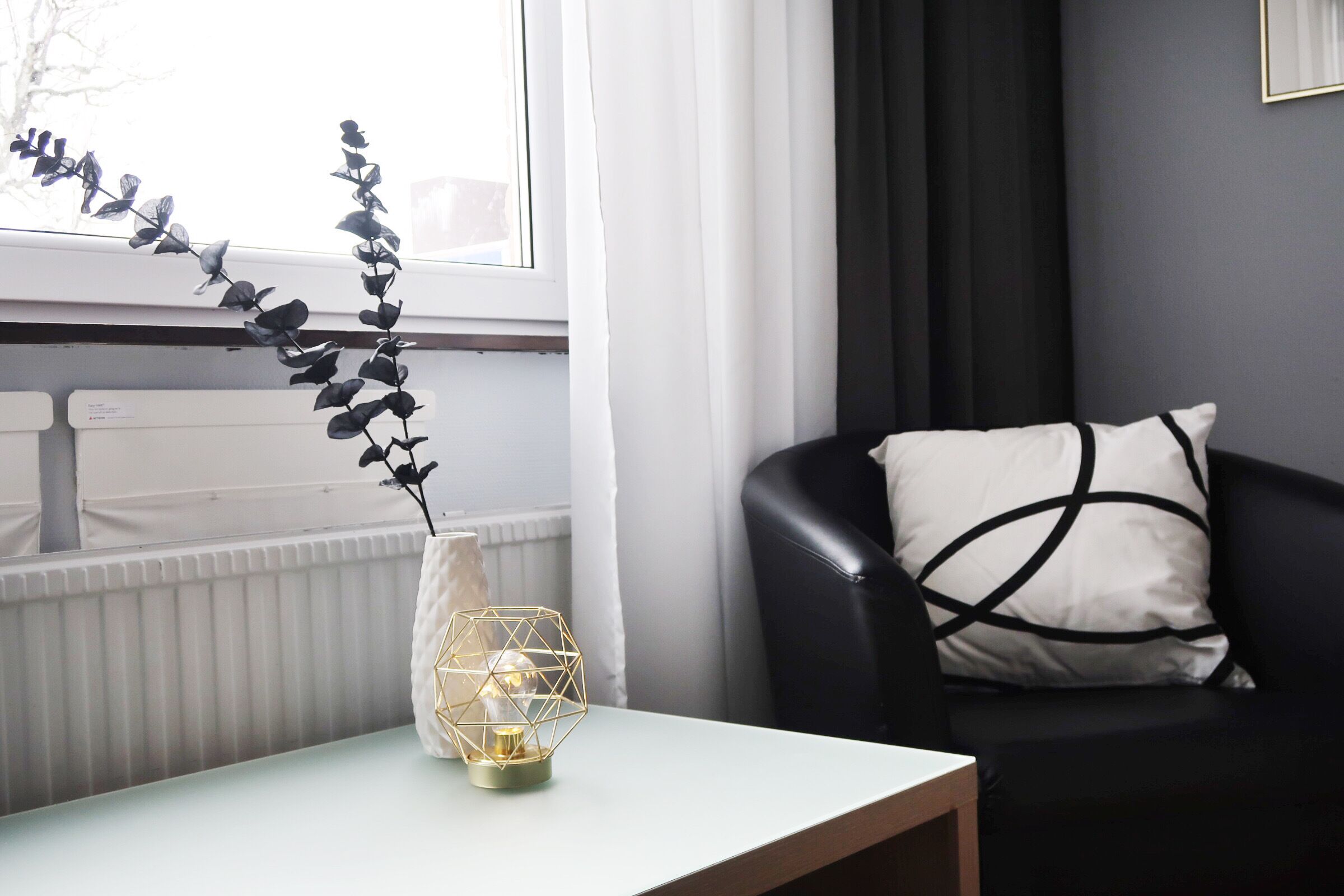 A modern living room with a white table, a black leather chair, and a decorative vase with a geometric design.