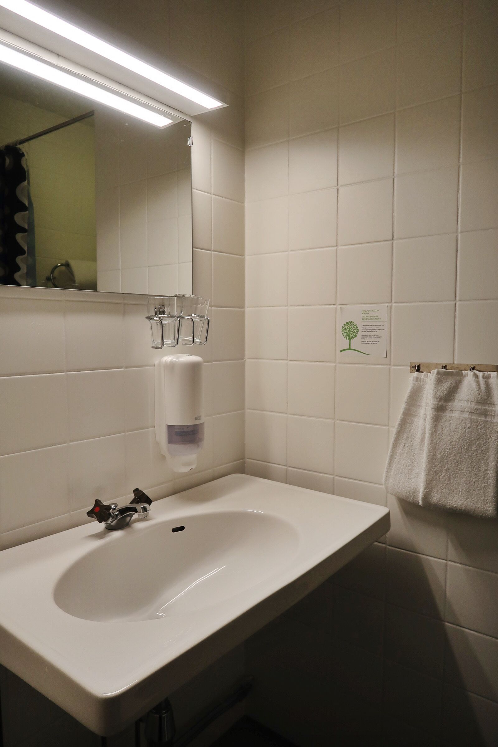 Ett badrum med ett vitt handfat, en spegel, en handdukshängare och en tvålpump.
